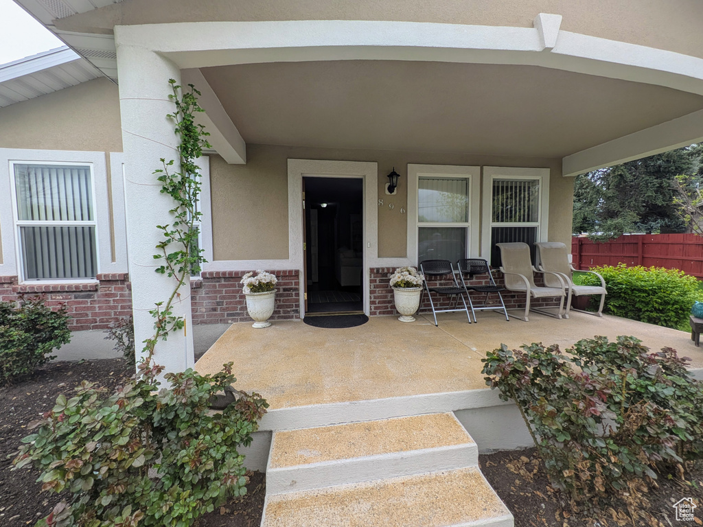 Property entrance featuring a porch, stucco siding, brick siding, and fence