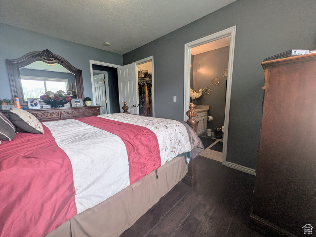Bedroom with a closet, a walk in closet, baseboards, ensuite bath, and dark wood-style floors