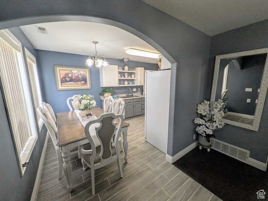 Dining space featuring wood finish floors, visible vents, an inviting chandelier, arched walkways, and baseboards