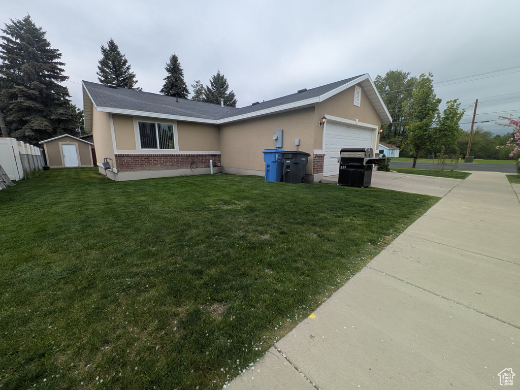 View of front of home with brick siding, an attached garage, concrete driveway, a front lawn, and a storage unit