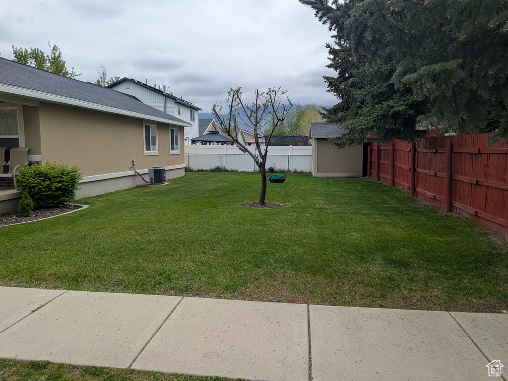 View of yard with a fenced backyard, an outdoor structure, a storage unit, and central AC
