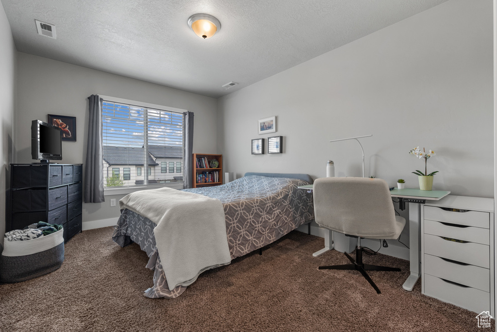 Bedroom with a textured ceiling, visible vents, baseboards, and dark carpet