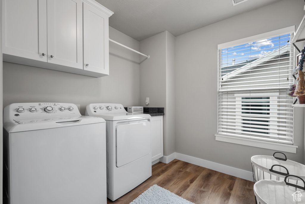 Clothes washing area with baseboards, separate washer and dryer, cabinet space, and wood finished floors