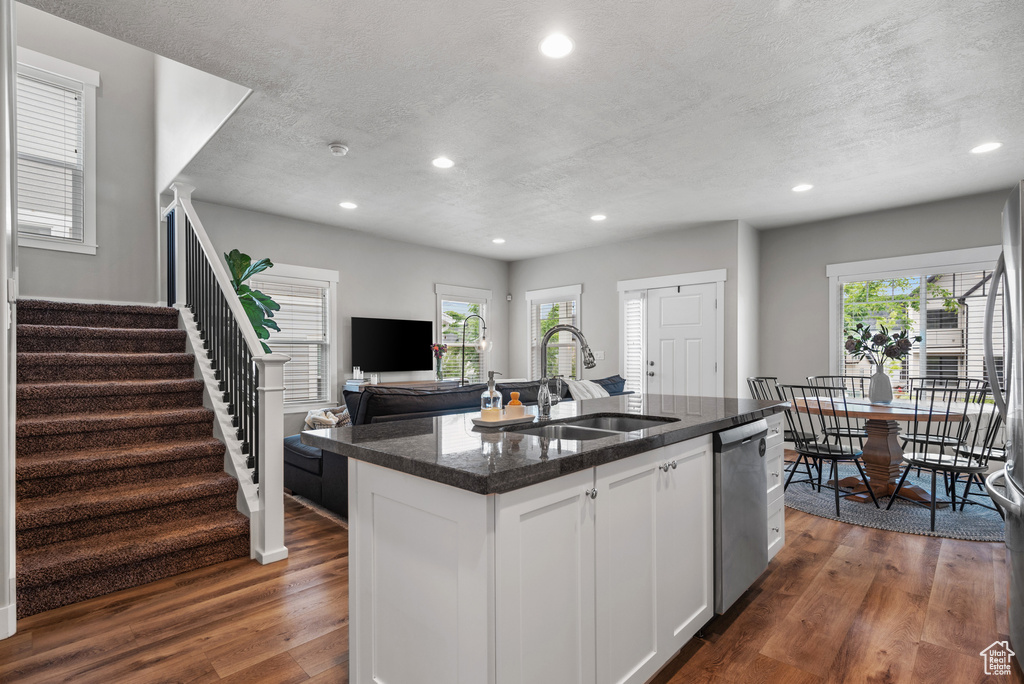 Kitchen with a sink, a kitchen island with sink, stainless steel dishwasher, dark wood-style flooring, and recessed lighting