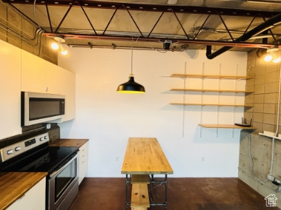 Kitchen with wooden counters, open shelves, stainless steel appliances, white cabinets, and concrete flooring
