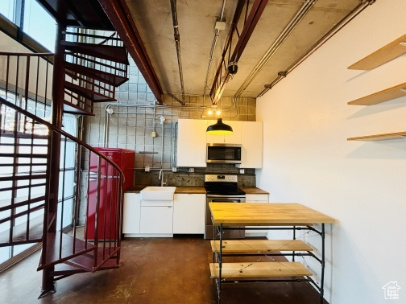 Kitchen with finished concrete flooring, a sink, white cabinetry, decorative backsplash, and stainless steel appliances