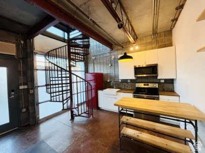 Kitchen with finished concrete flooring, a sink, white cabinetry, tasteful backsplash, and appliances with stainless steel finishes