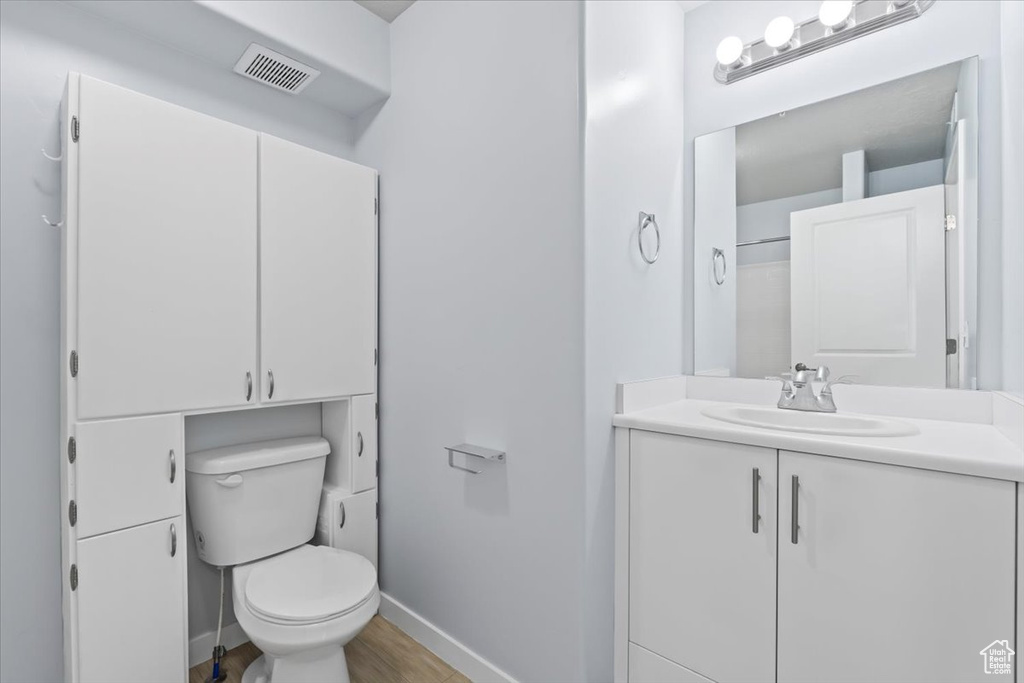 Bathroom with toilet, baseboards, visible vents, vanity, and wood finished floors