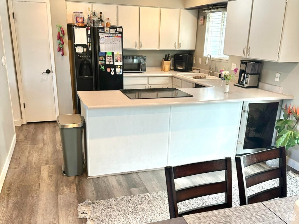 Kitchen with a sink, a peninsula, black appliances, light countertops, and light wood-style floors