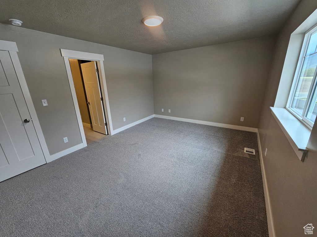 Unfurnished room with a textured ceiling, carpet floors, baseboards, and visible vents