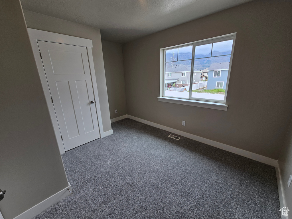Unfurnished bedroom featuring a textured ceiling, visible vents, baseboards, and carpet floors