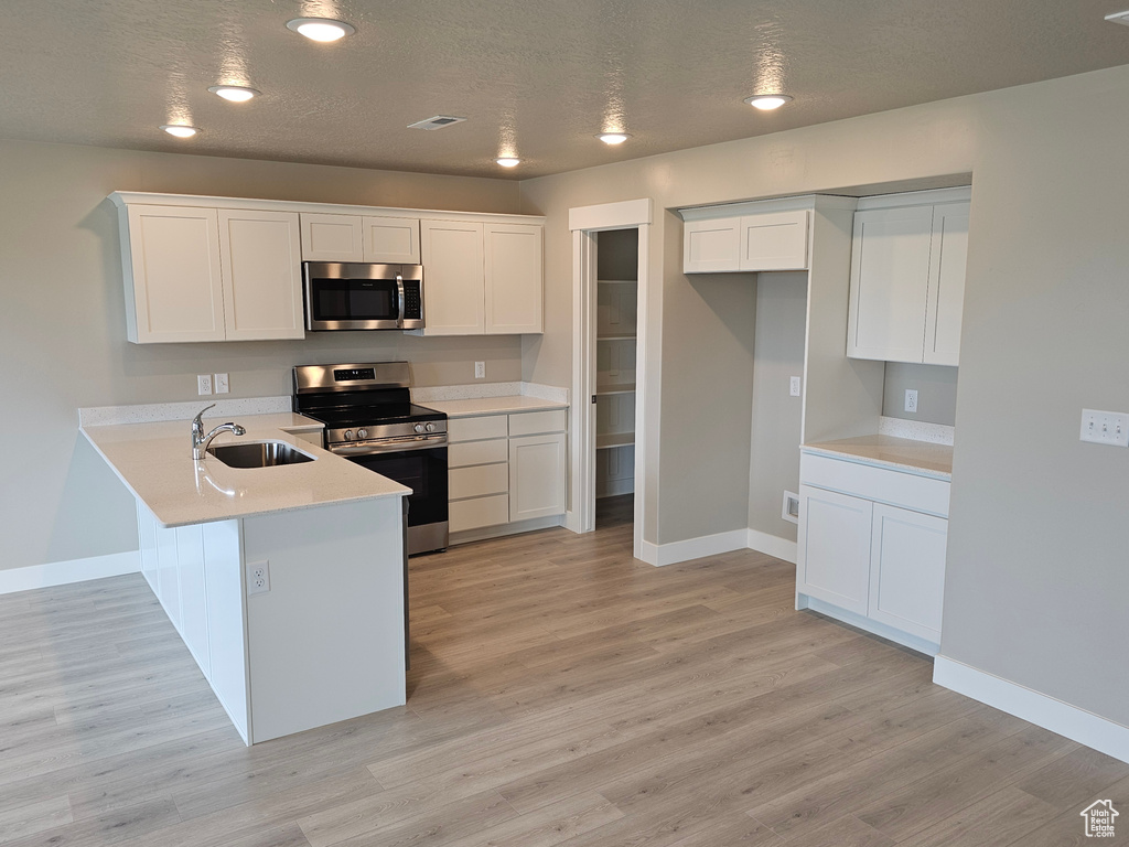 Kitchen with visible vents, a sink, white cabinetry, a peninsula, and stainless steel appliances
