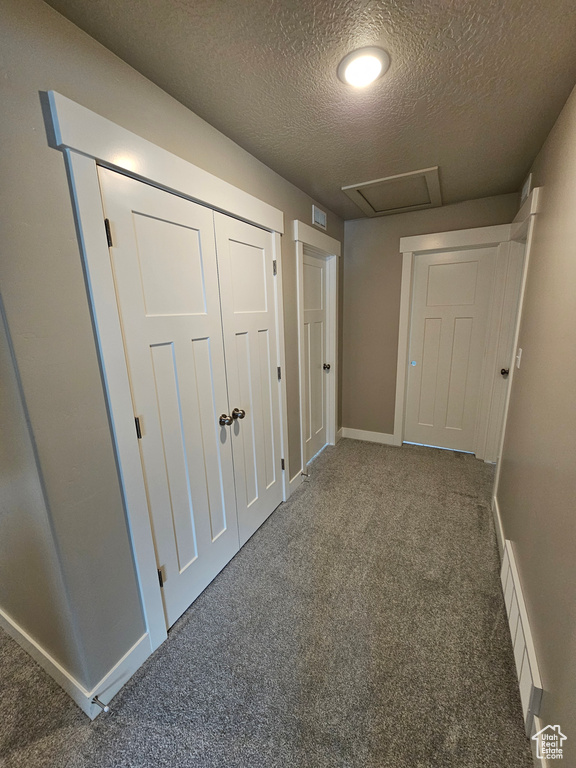 Corridor featuring carpet, attic access, a textured ceiling, visible vents, and baseboards