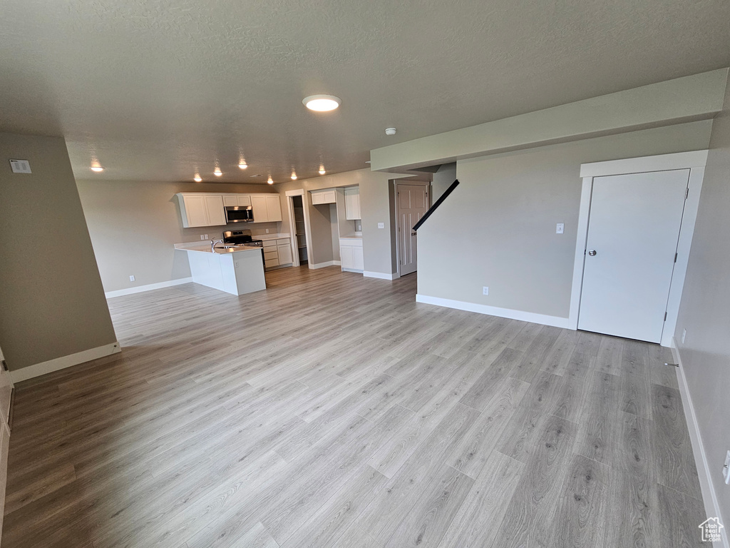 Unfurnished living room featuring light wood-type flooring, baseboards, stairs, and a textured ceiling