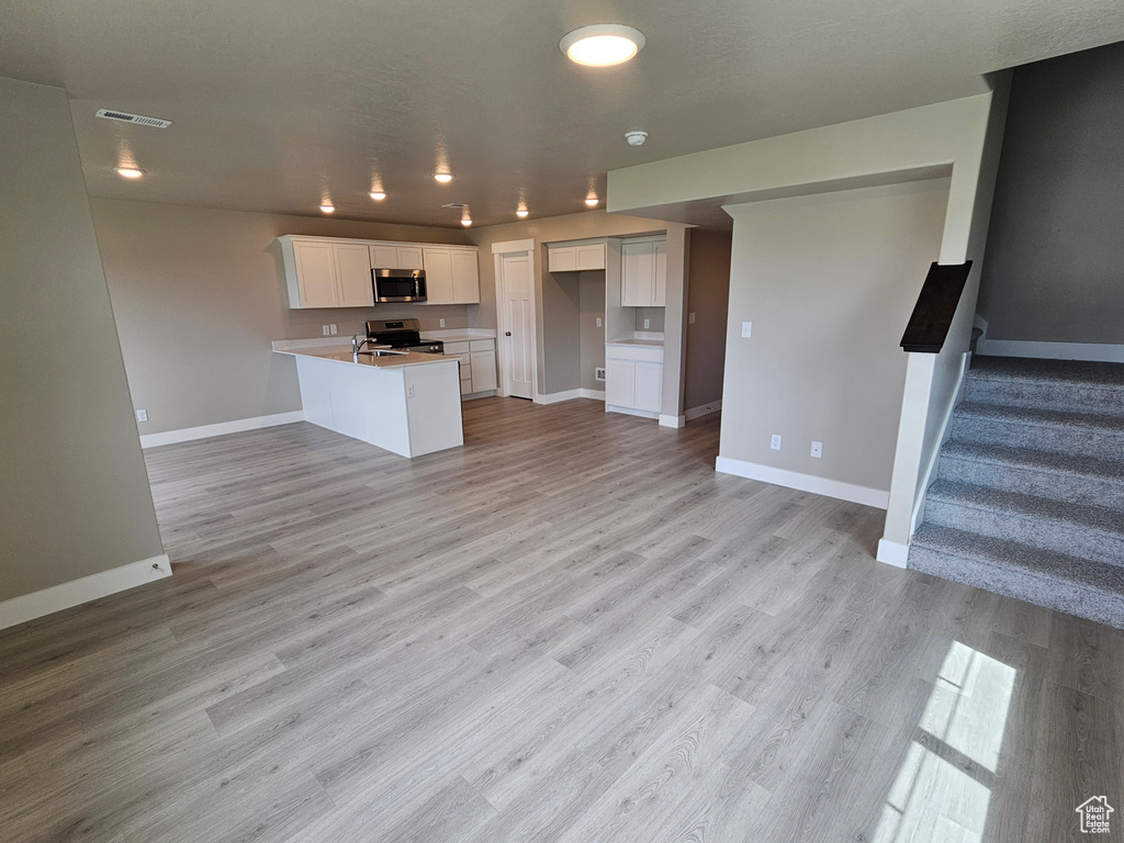 Kitchen featuring a peninsula, stainless steel appliances, visible vents, open floor plan, and baseboards