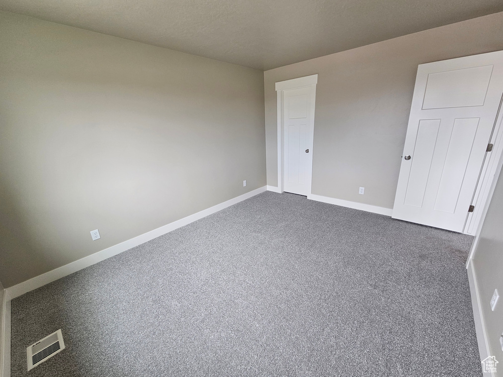 Empty room with baseboards, dark colored carpet, and visible vents