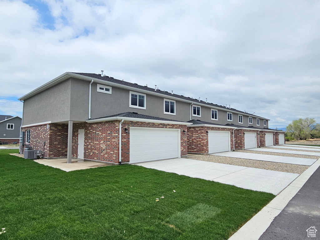 View of property featuring an attached garage, stucco siding, concrete driveway, central AC unit, and a front yard