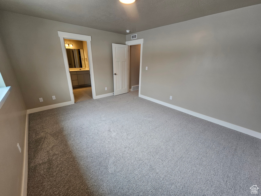 Unfurnished bedroom featuring a textured ceiling, baseboards, visible vents, connected bathroom, and carpet floors
