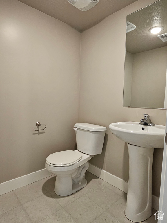 Half bathroom featuring toilet, visible vents, baseboards, and a textured ceiling
