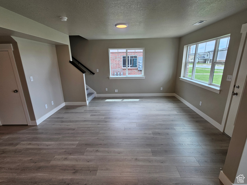 Unfurnished living room with a textured ceiling, stairs, visible vents, and wood finished floors