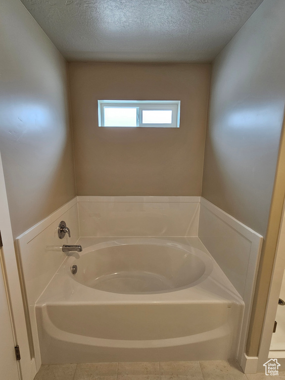 Full bath with a textured ceiling, a garden tub, and tile patterned floors