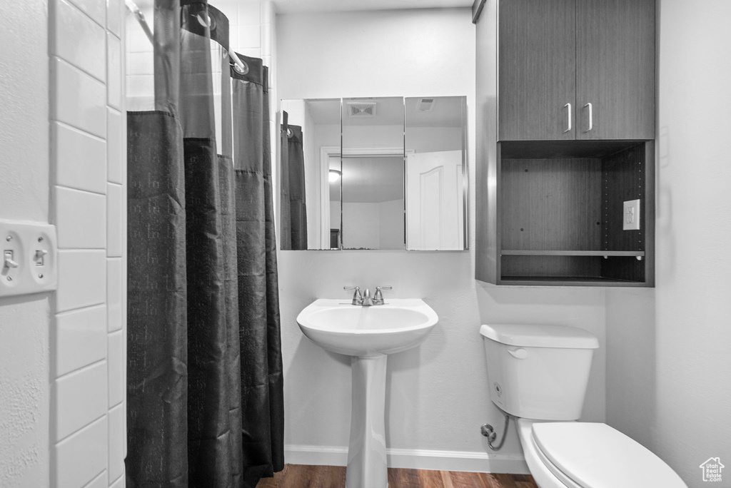 Bathroom featuring toilet, curtained shower, wood finished floors, and baseboards