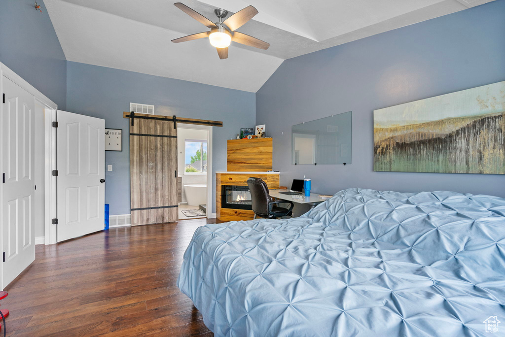 Bedroom with a barn door, wood finished floors, visible vents, and vaulted ceiling