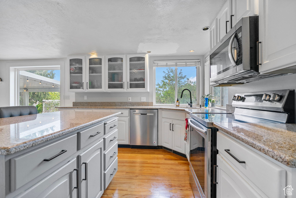Kitchen with glass insert cabinets, light wood-style flooring, a sink, white cabinets, and appliances with stainless steel finishes
