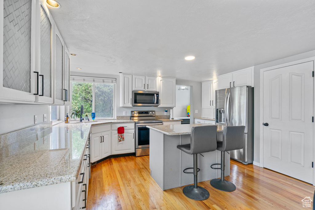 Kitchen with a kitchen island, light wood-style floors, stainless steel appliances, and white cabinetry