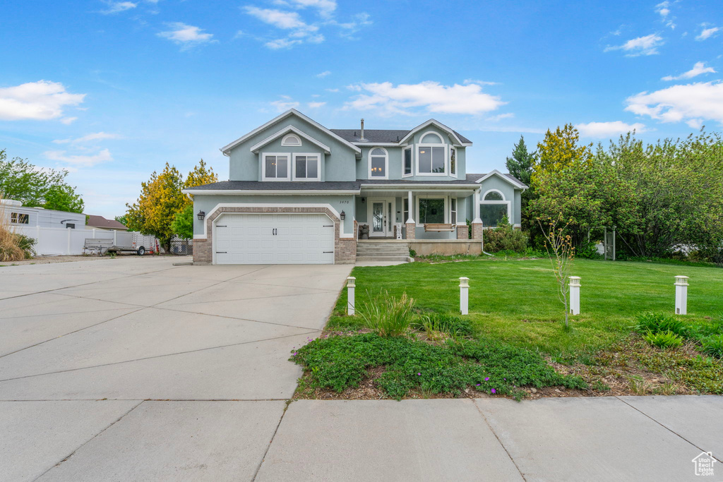 View of front of home with driveway, an attached garage, stucco siding, a porch, and a front lawn