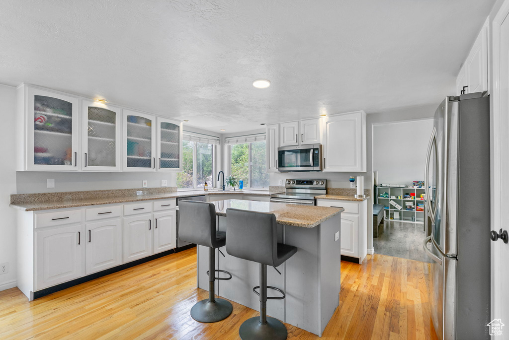 Kitchen with a sink, stainless steel appliances, white cabinetry, a center island, and light wood-style floors