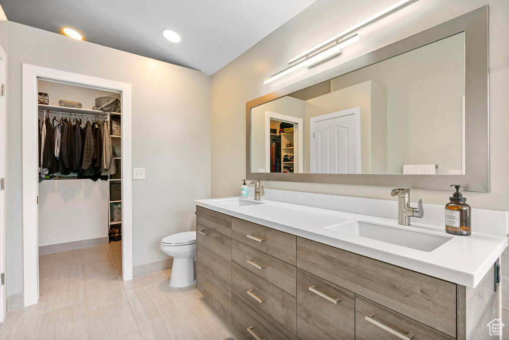 Full bathroom with double vanity, toilet, baseboards, and a sink