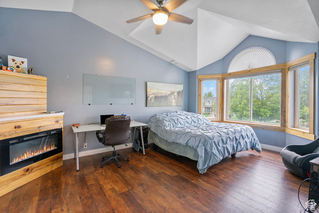 Bedroom featuring lofted ceiling, baseboards, a glass covered fireplace, and hardwood / wood-style flooring