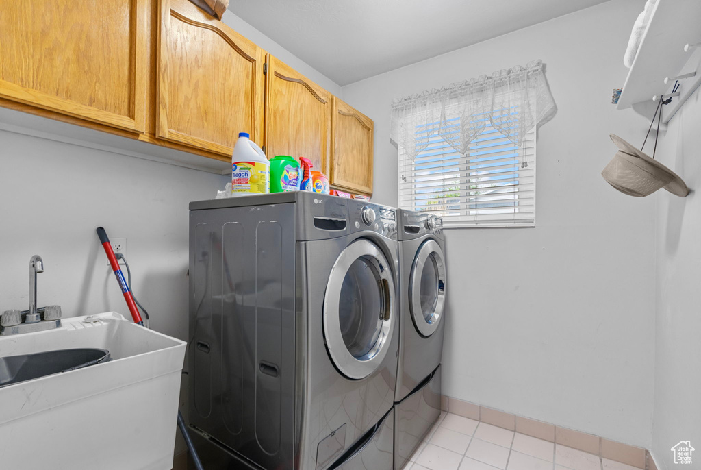 Clothes washing area with washing machine and clothes dryer, a sink, light tile patterned floors, and cabinet space