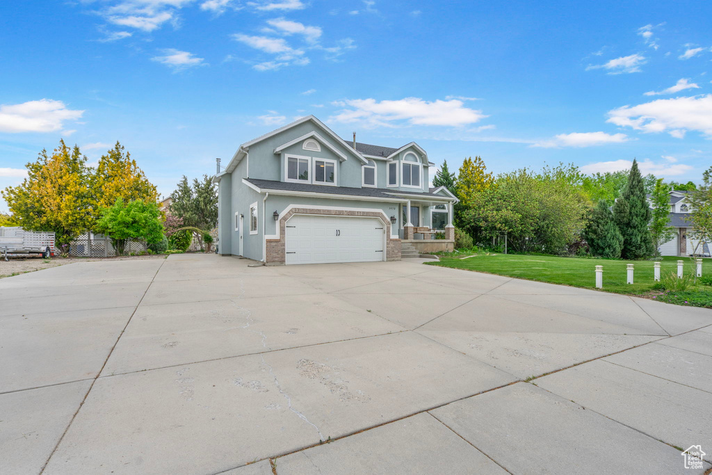 View of front of house featuring driveway, brick siding, an attached garage, stucco siding, and a front yard