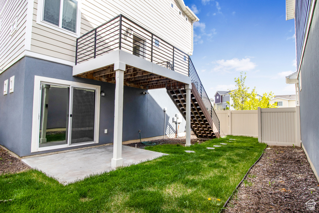 Rear view of house with fence, stairs, stucco siding, a lawn, and a patio