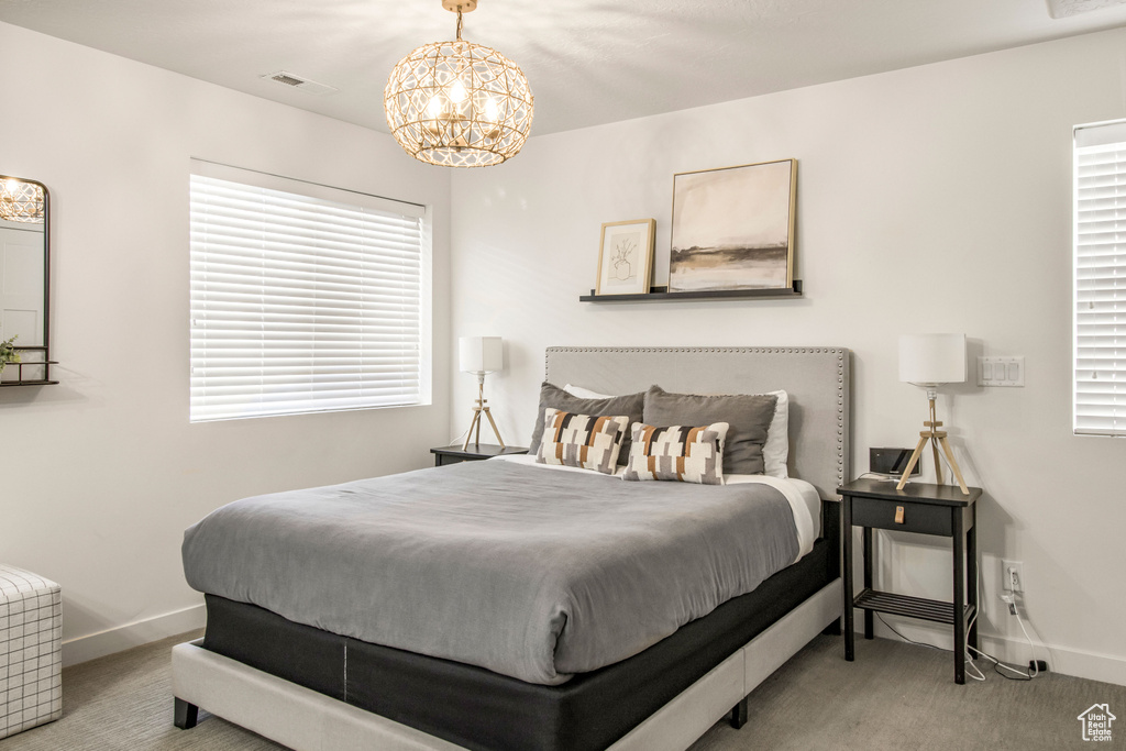 Carpeted bedroom featuring baseboards, visible vents, multiple windows, and a chandelier