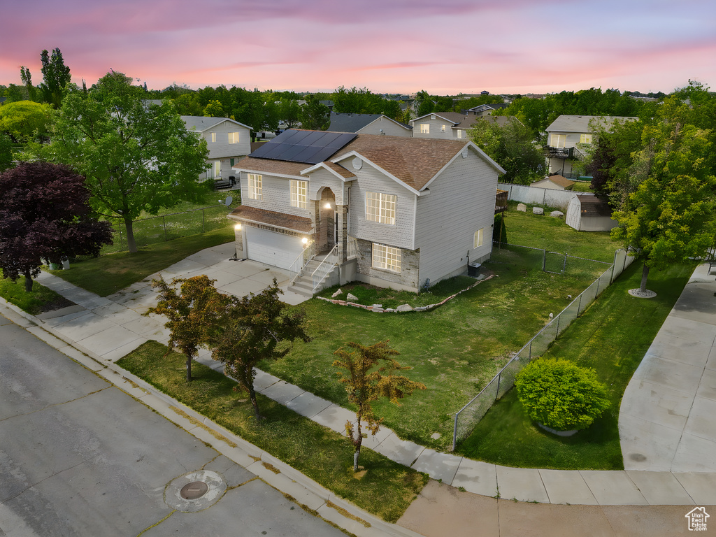 View of front facade with an attached garage, roof mounted solar panels, a lawn, a fenced backyard, and driveway
