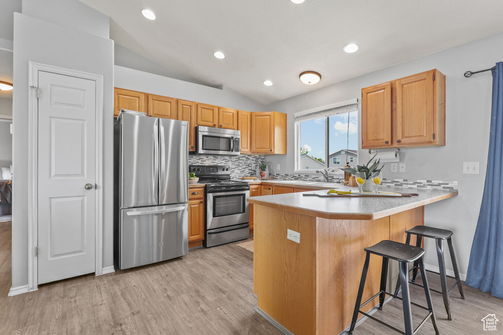 Kitchen with a peninsula, stainless steel appliances, light wood-type flooring, vaulted ceiling, and tasteful backsplash