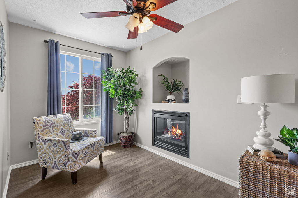 Living area with a ceiling fan, wood finished floors, baseboards, and a glass covered fireplace