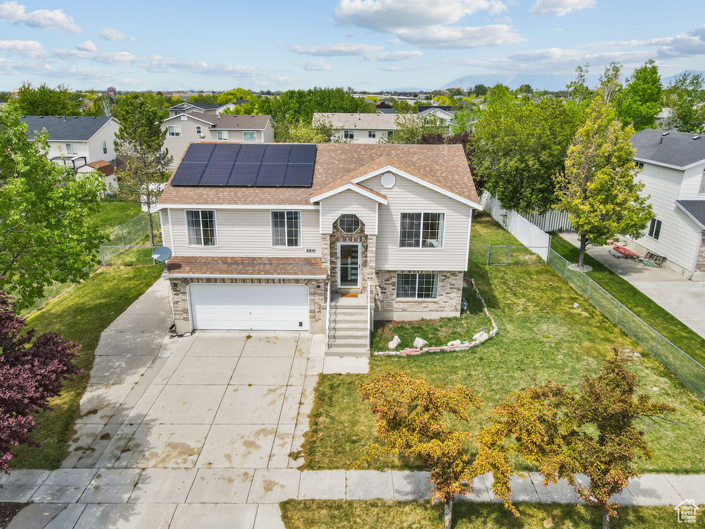 Raised ranch with a residential view, a garage, solar panels, a front yard, and driveway