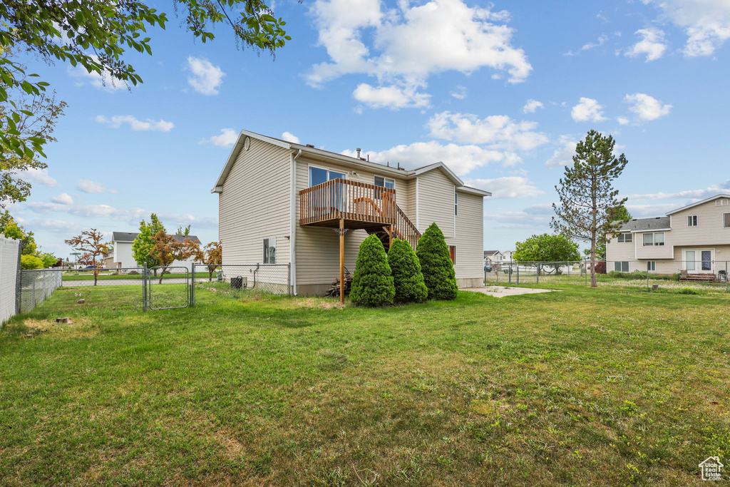 Rear view of house featuring a lawn, a wooden deck, a fenced backyard, and a gate