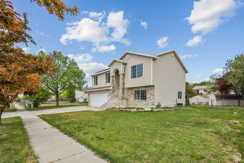 Split level home with concrete driveway, a garage, a front lawn, and fence