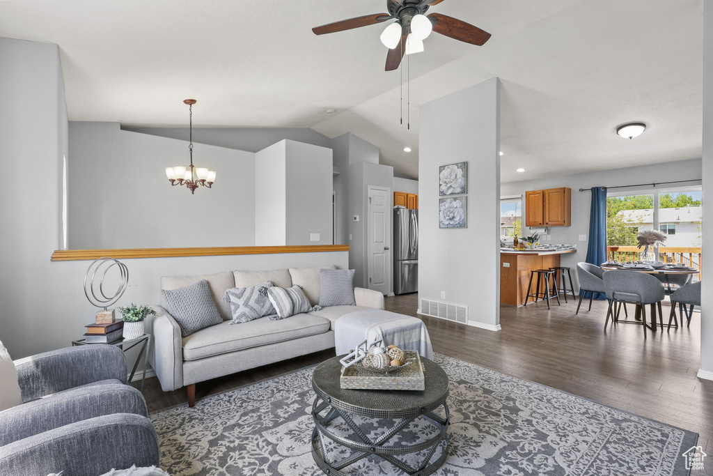Living area with ceiling fan with notable chandelier, dark wood-type flooring, visible vents, vaulted ceiling, and baseboards