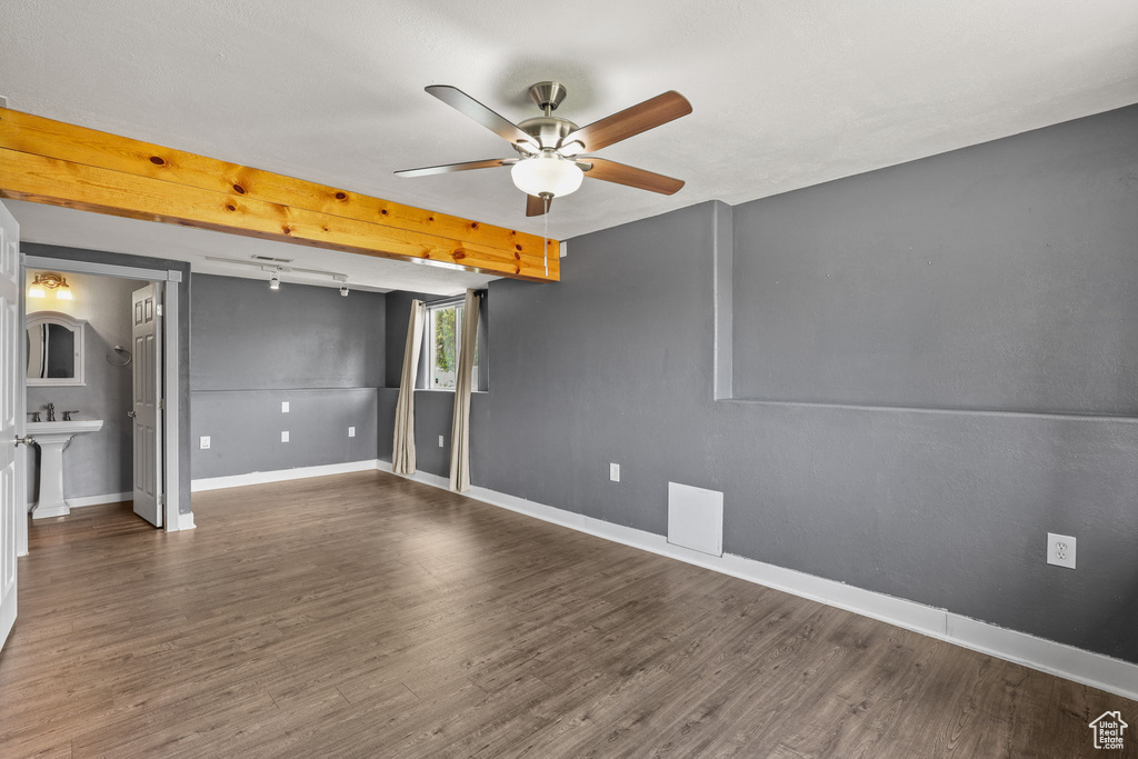 Unfurnished room featuring a sink, beam ceiling, wood finished floors, a ceiling fan, and baseboards