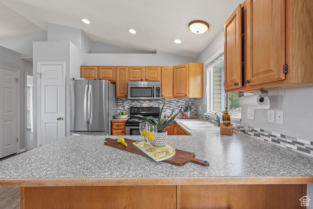 Kitchen with stainless steel appliances, a peninsula, a sink, and vaulted ceiling