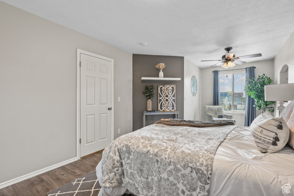 Bedroom with a textured ceiling, dark wood-style flooring, baseboards, and ceiling fan