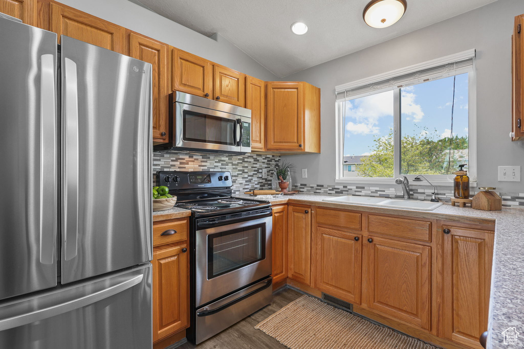 Kitchen featuring lofted ceiling, stainless steel appliances, dark wood-style flooring, light countertops, and tasteful backsplash