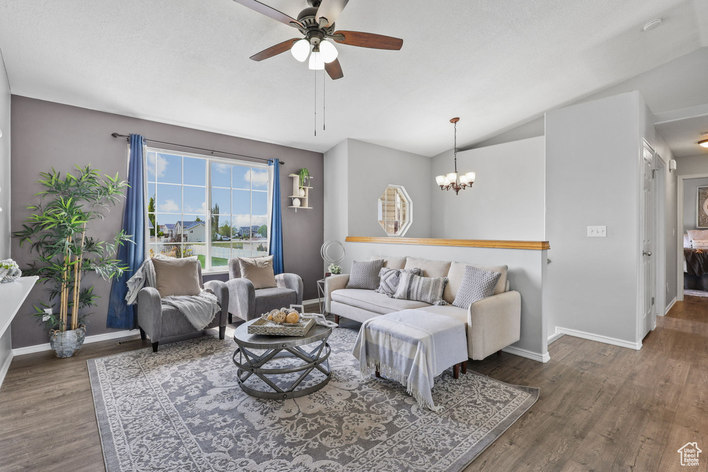 Living area with vaulted ceiling, ceiling fan with notable chandelier, baseboards, and wood finished floors