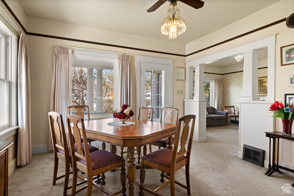Dining space with light carpet, a ceiling fan, visible vents, and decorative columns